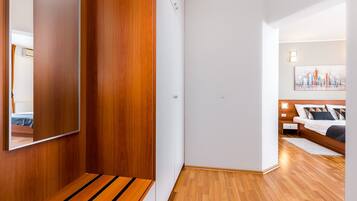 A modern hotel room with a wooden floor, a bed with a white headboard, a nightstand, and a wall-mounted mirror.