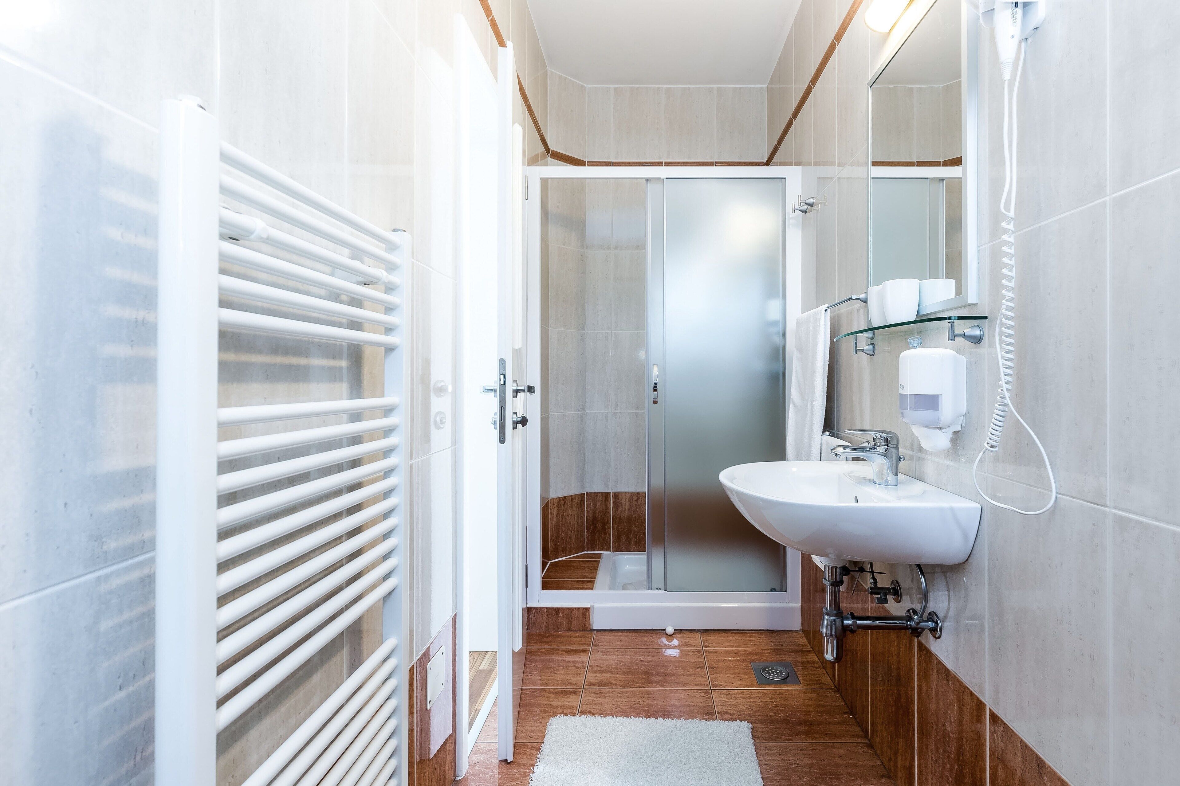 A modern bathroom with a glass shower enclosure, a white sink, and a glass shelf with toiletries.