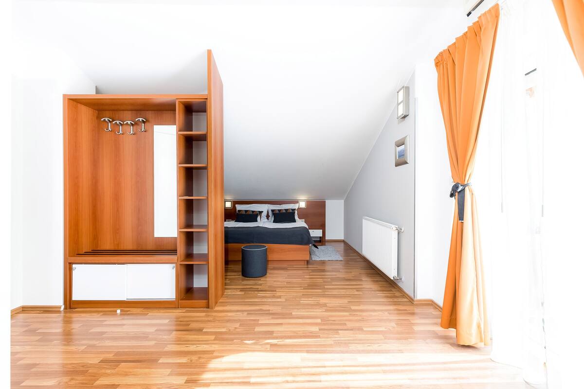 A bedroom with a loft bed, wooden wardrobe, and a small trash bin.