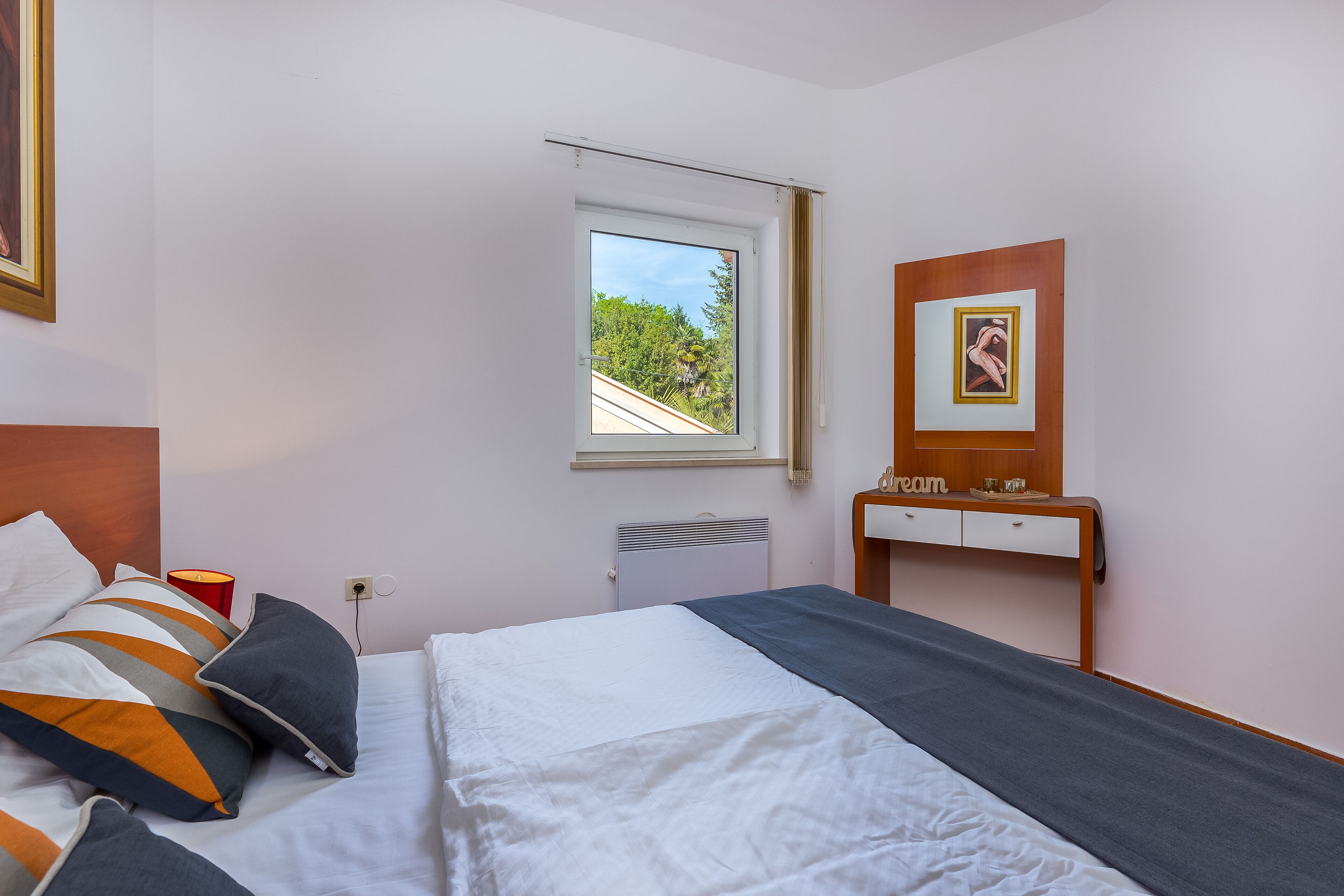 Een keurig opgemaakt slaapkamer met een bed, nachtkastje en een raam met uitzicht op groen.