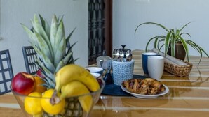 Et spisebord med en skål frugt, en tallerken mad og en kaffekande.