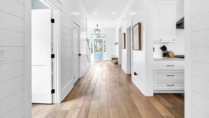 A hallway with white paneling, wooden flooring, and a view into a room with a blue door.