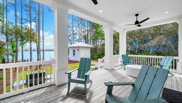 A covered porch with Adirondack chairs, a grill, and a view of a lake and trees.