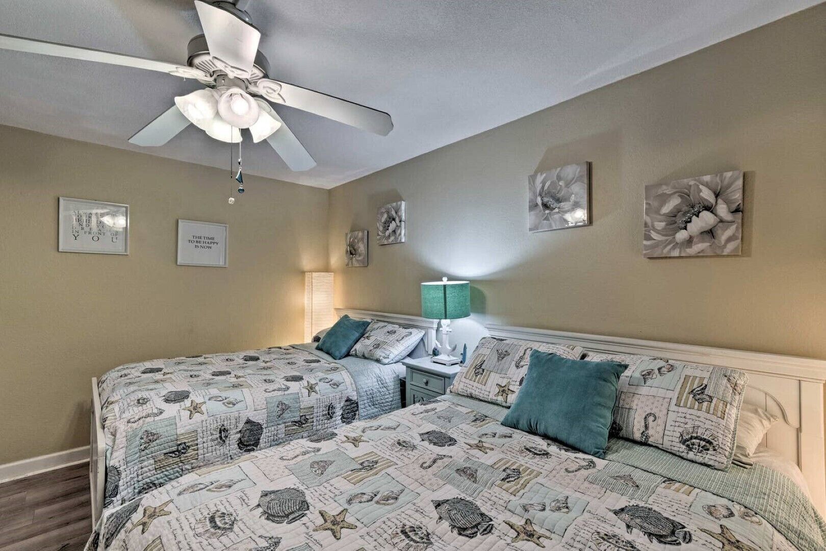 Une chambre avec deux lits, un ventilateur de plafond et des œuvres d’art murales.