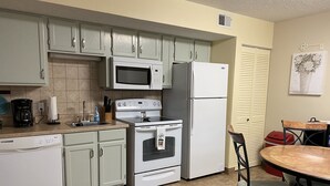 A kitchen with light green cabinets, a white refrigerator, a microwave, a stove, and a dining table with chairs. - At home feeling with amenities. (Branson)