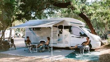 Un camper con una zona giorno riparata, due persone sedute all'interno e un'altra persona all'esterno.