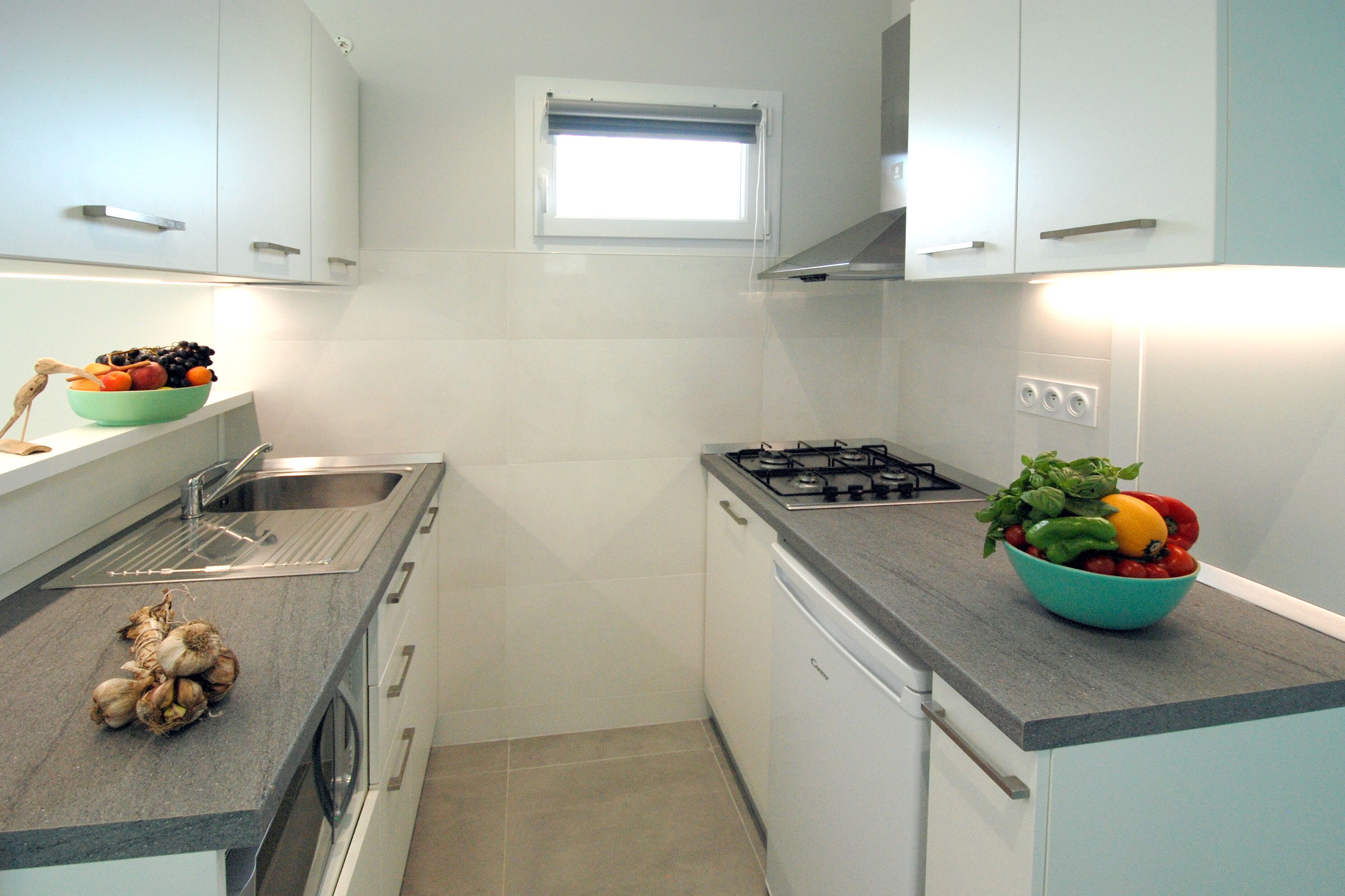 Een kleine keuken met witte kastjes, een gasfornuis, een spoelbak en een raam boven het aanrecht.