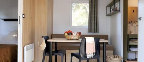 Una habitación compacta con cama, una pequeña mesa con sillas, un ventanal con cortinas y un estante con artículos de aseo.
