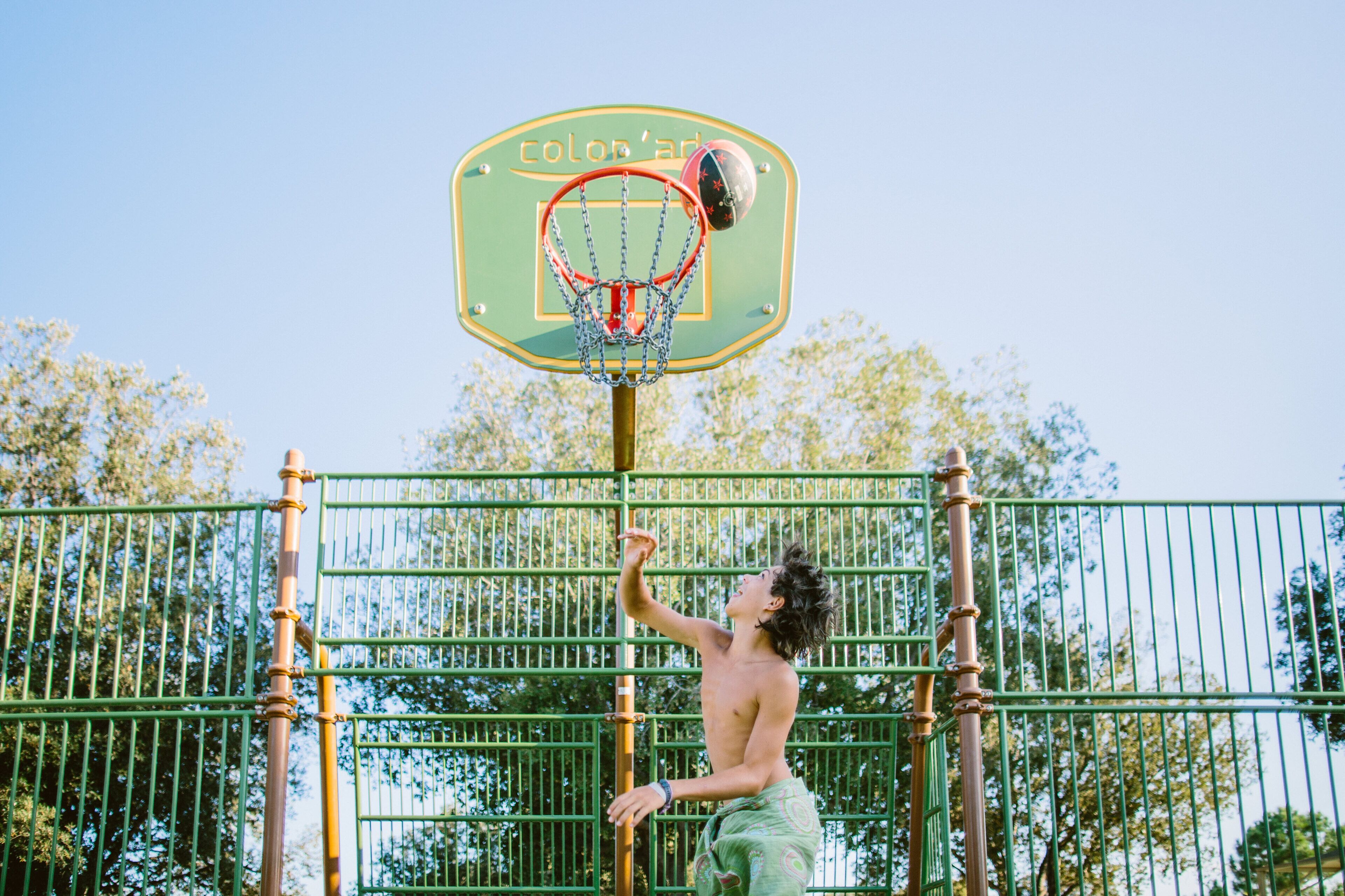 A basketball hoop with a sign that reads "colob'Art" in front of a green metal fence.