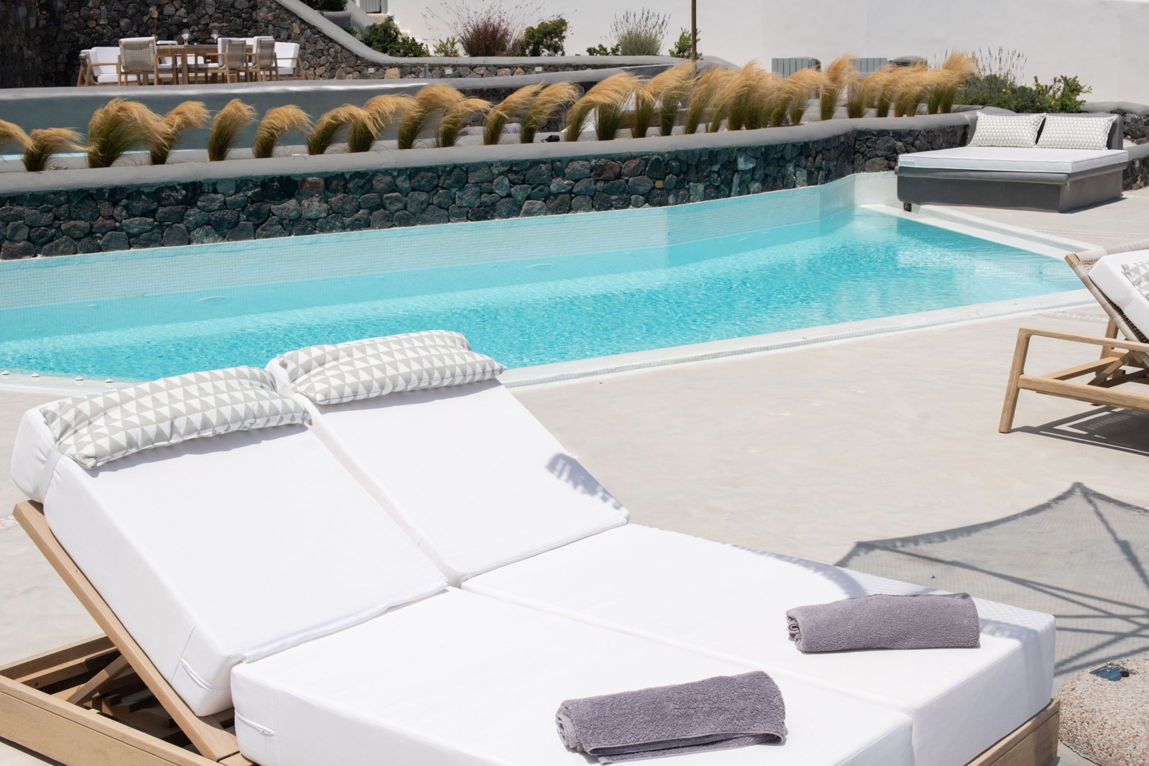 A poolside area with lounge chairs, a stone wall, and a view of the pool.