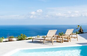 Ein Poolbereich mit zwei Holzliegen, die Blick auf das klare Meer bieten.