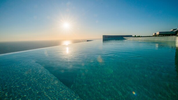 A clear infinity pool with a view of the ocean and a building in the background. - Aregou Villas (Santorini)