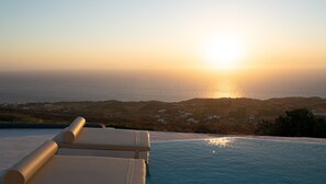 Blick auf einen Pool mit Sonnenuntergang über dem Meer, bewölkter Himmel und Küste in der Ferne.