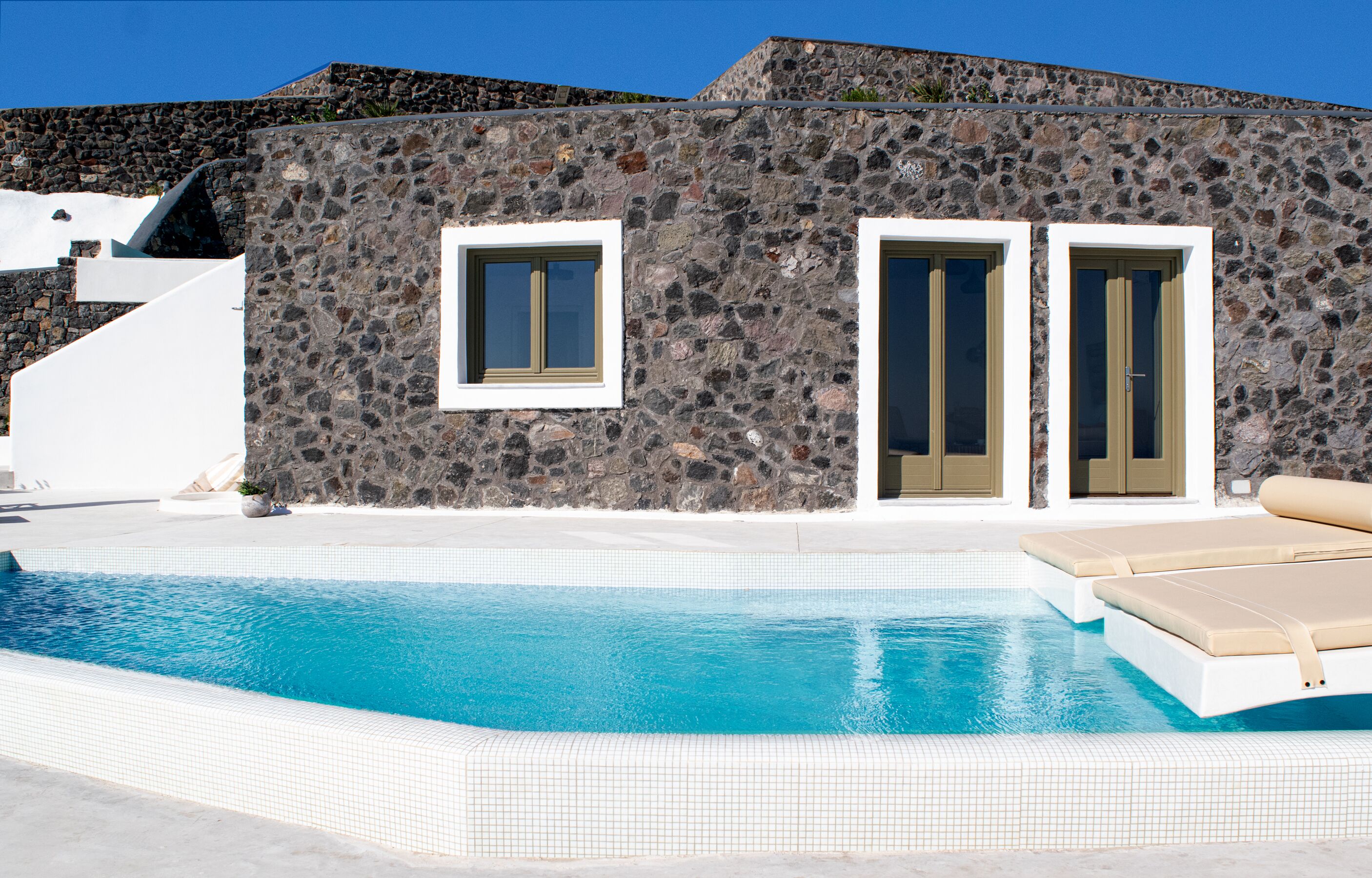A stone building with a swimming pool, two doors, and a white exterior.