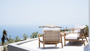 A terrace with wicker chairs and a table, overlooking a clear blue sea. - Aregou Villas (Santorini)