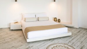 A minimalist bedroom with a bed, bedside tables, and pendant lights. - Aregou Villas (Santorini)