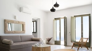 A modern living room with a sofa, a round wooden coffee table, a wicker chair, and a large mirror on the wall. - Aregou Villas (Santorini)
