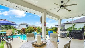 Un espace extérieur aménagé en terrasse, avec une table ronde, des chaises, un barbecue et une piscine en arrière-plan.