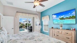 Une chambre avec un lit, un ventilateur de plafond, une télévision et une vue sur une piscine et une maison à l’extérieur.