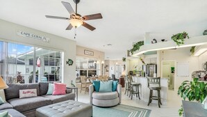 Un vaste espace de vie comprenant un canapé, un pouf et un ventilateur de plafond.