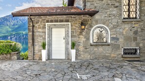 Un bâtiment en pierre avec un toit recouvert de tuiles, une porte blanche et une petite fenêtre ornée d’un cadre décoratif.