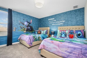A bedroom with two beds, a wall mural, and a window with curtains.