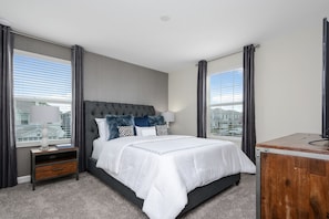 Un dormitorio moderno con una cama grande, una mesita de noche, un aparador de madera y vistas a la ciudad a través de amplios ventanales.