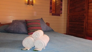 Una cama con cubrecama azul, dos almohadas y dos toallas enrolladas.
