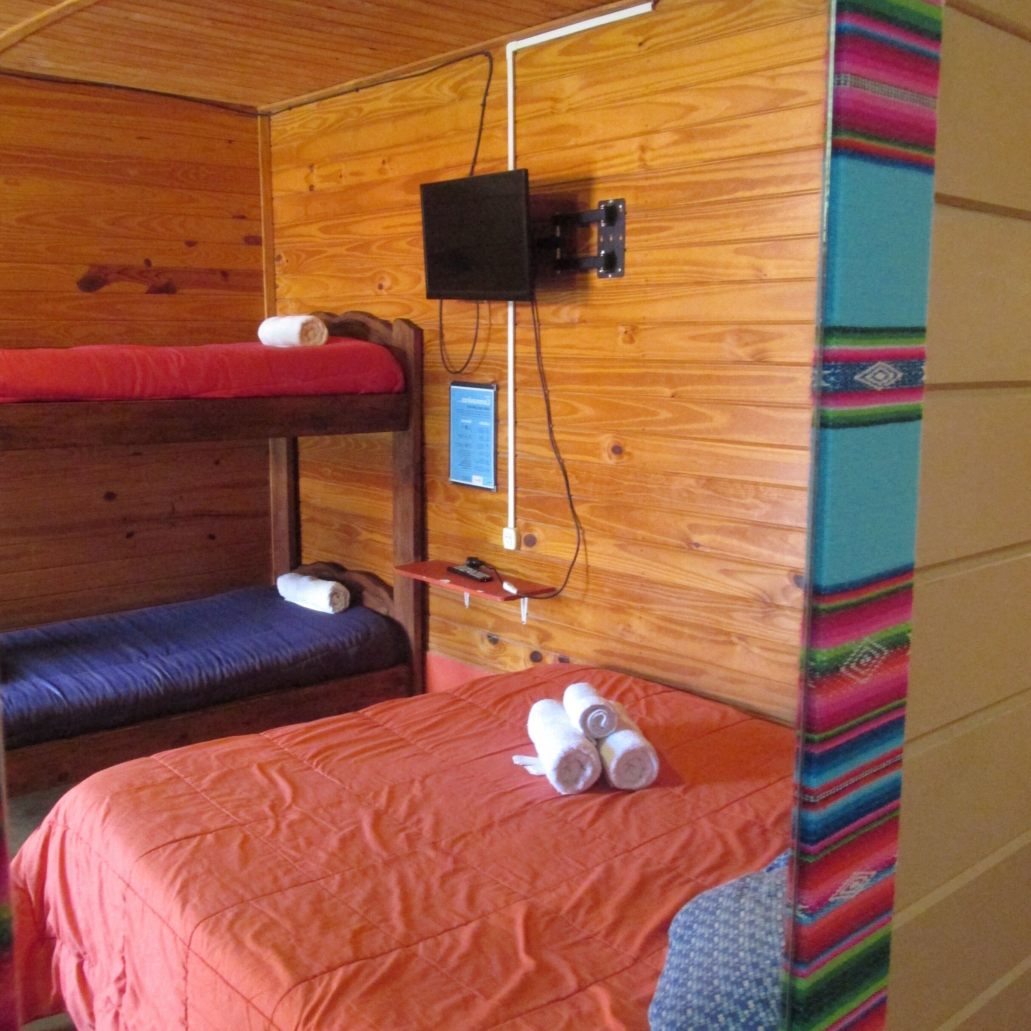 A room with two bunk beds, a television mounted on the wall, and a colorful blanket draped over the right side.