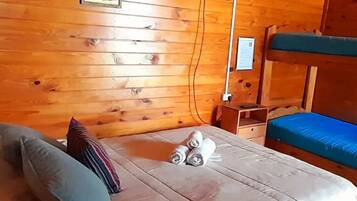 A wooden-paneled room with a bed, a television mounted on the wall, and a bunk bed.