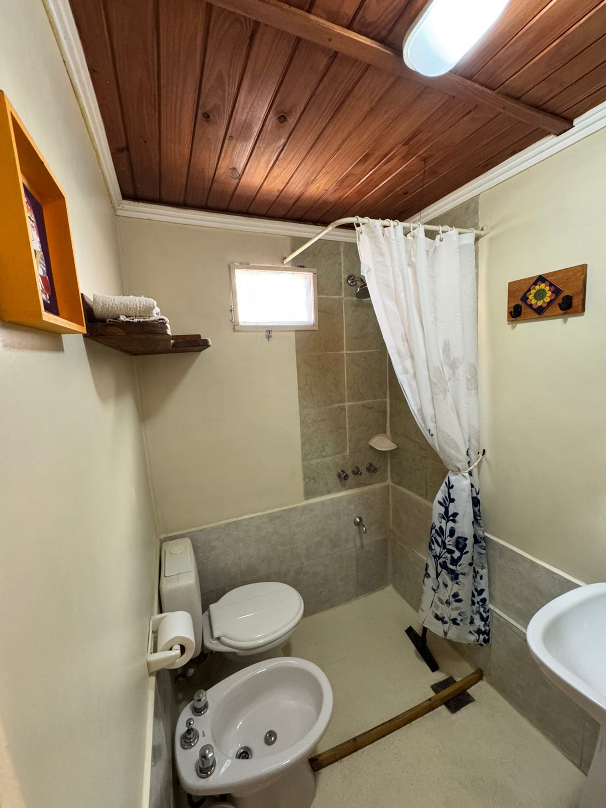 A small bathroom with a wooden ceiling, a shower, a toilet, a bidet, and a sink.
