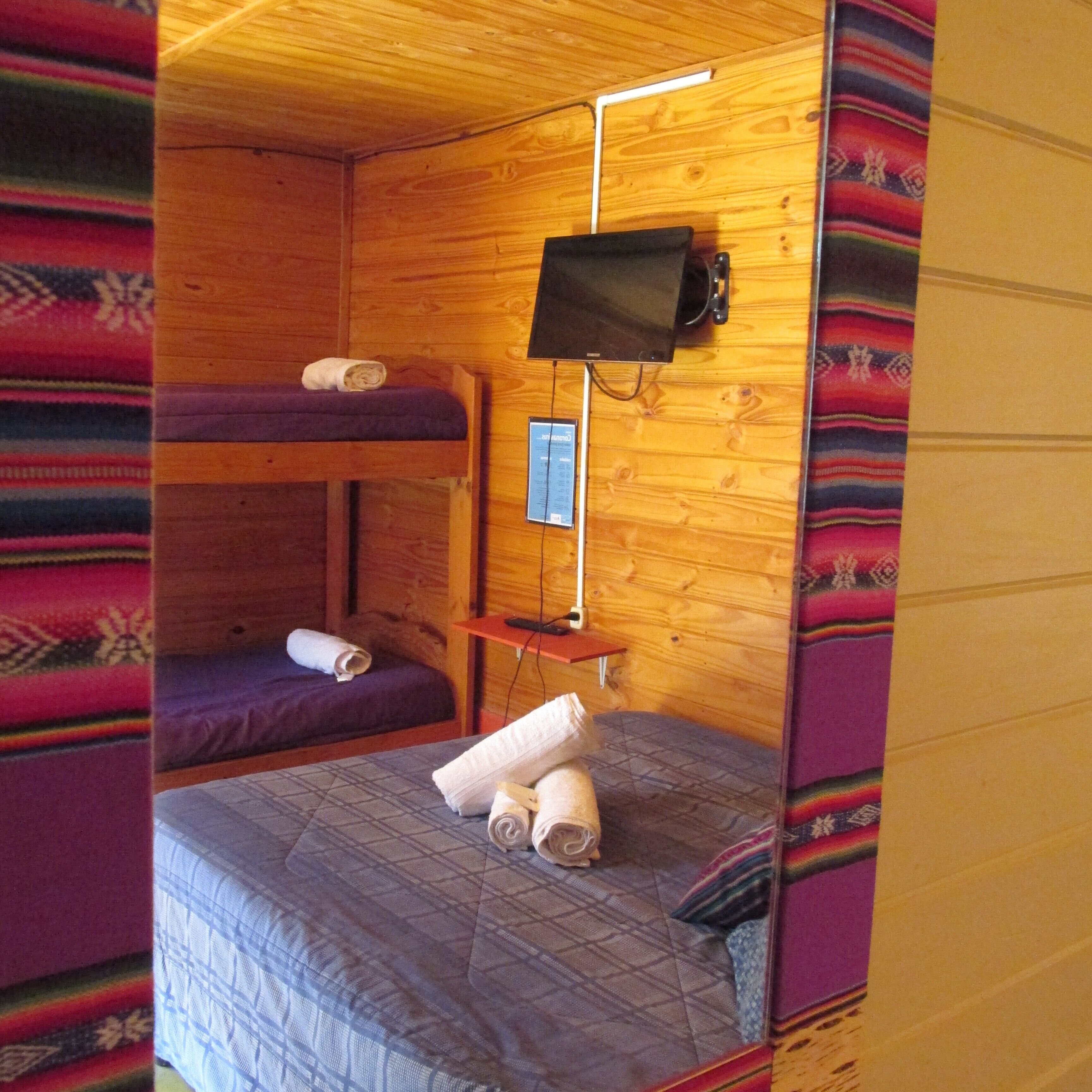Habitación de cabaña de madera con literas, televisión y una pequeña mesa.