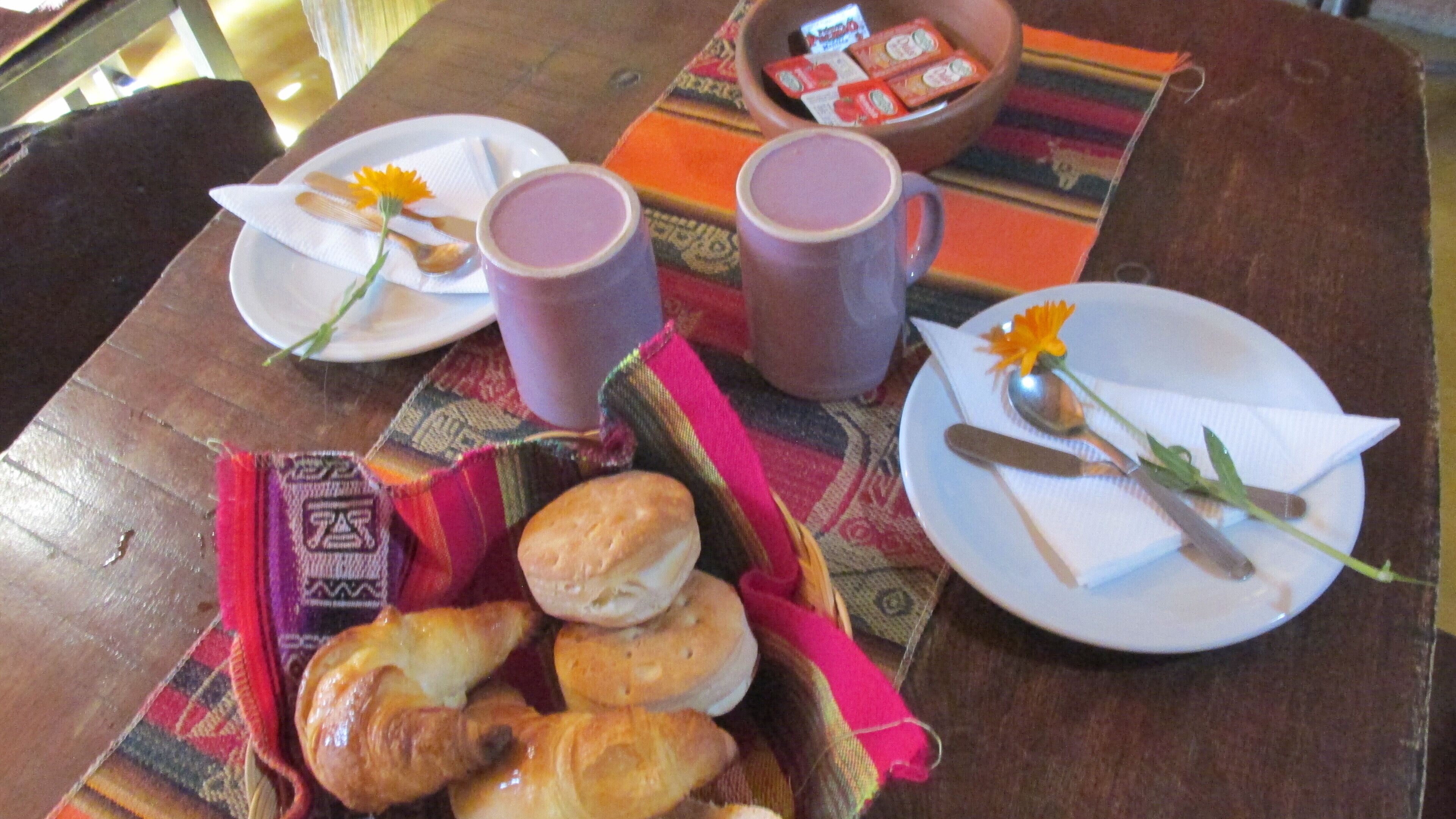A table with plates, cups, and a basket of pastries.