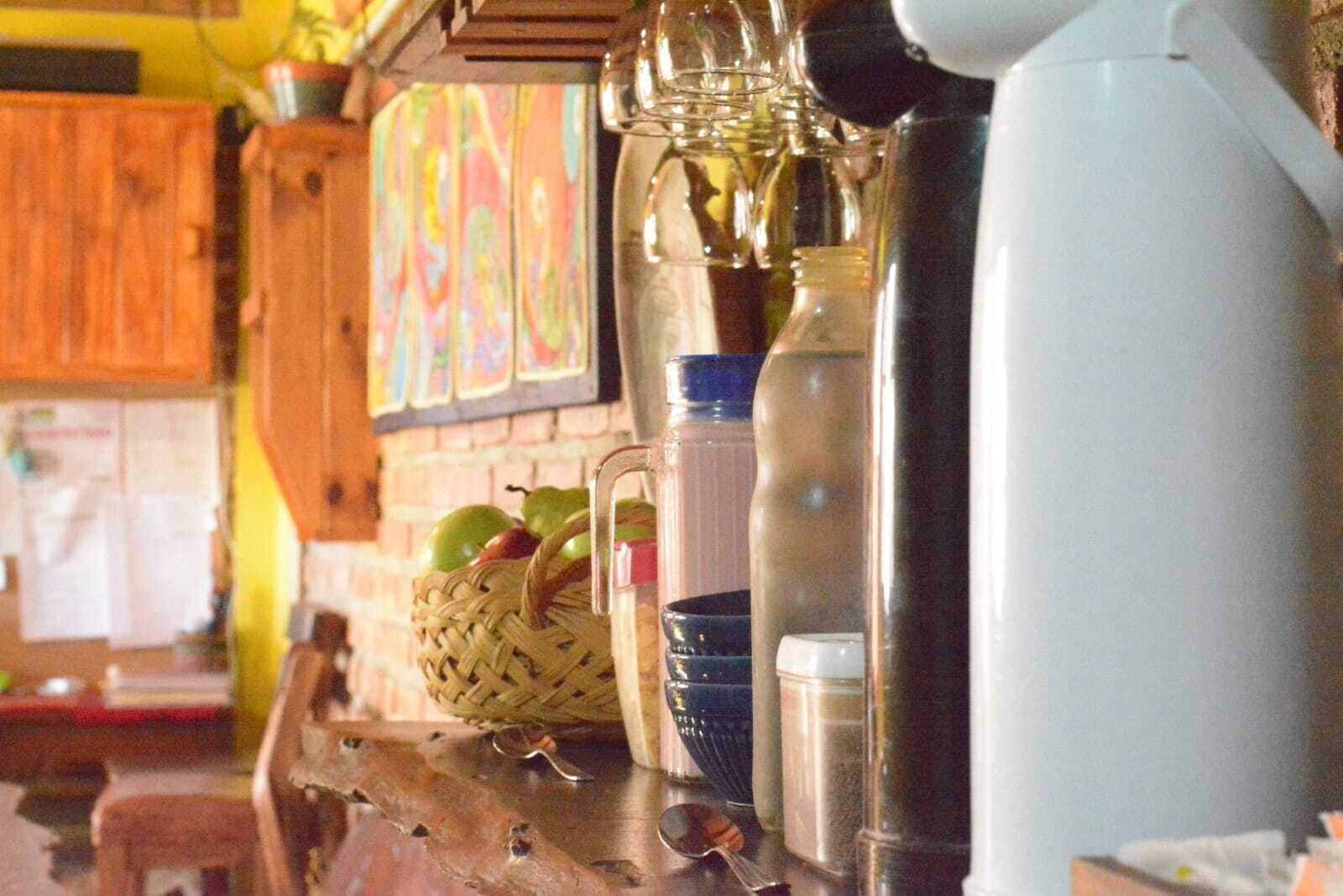 A kitchen counter with various items including a coffee maker, a water bottle, a basket with apples, and a blue bowl.