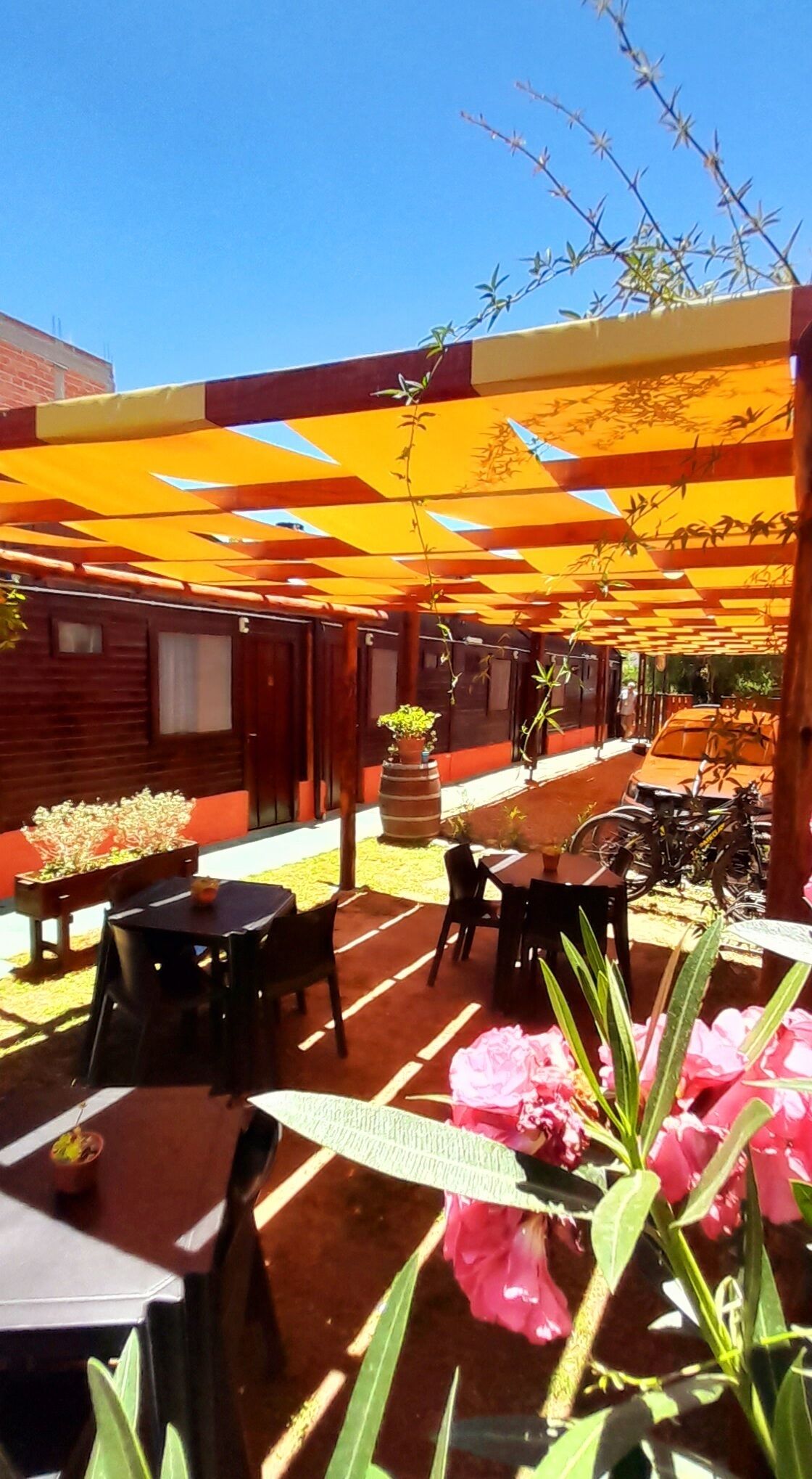 Un área de patio al aire libre con mesas y sillas, una zona de estar techada y un edificio al fondo.
