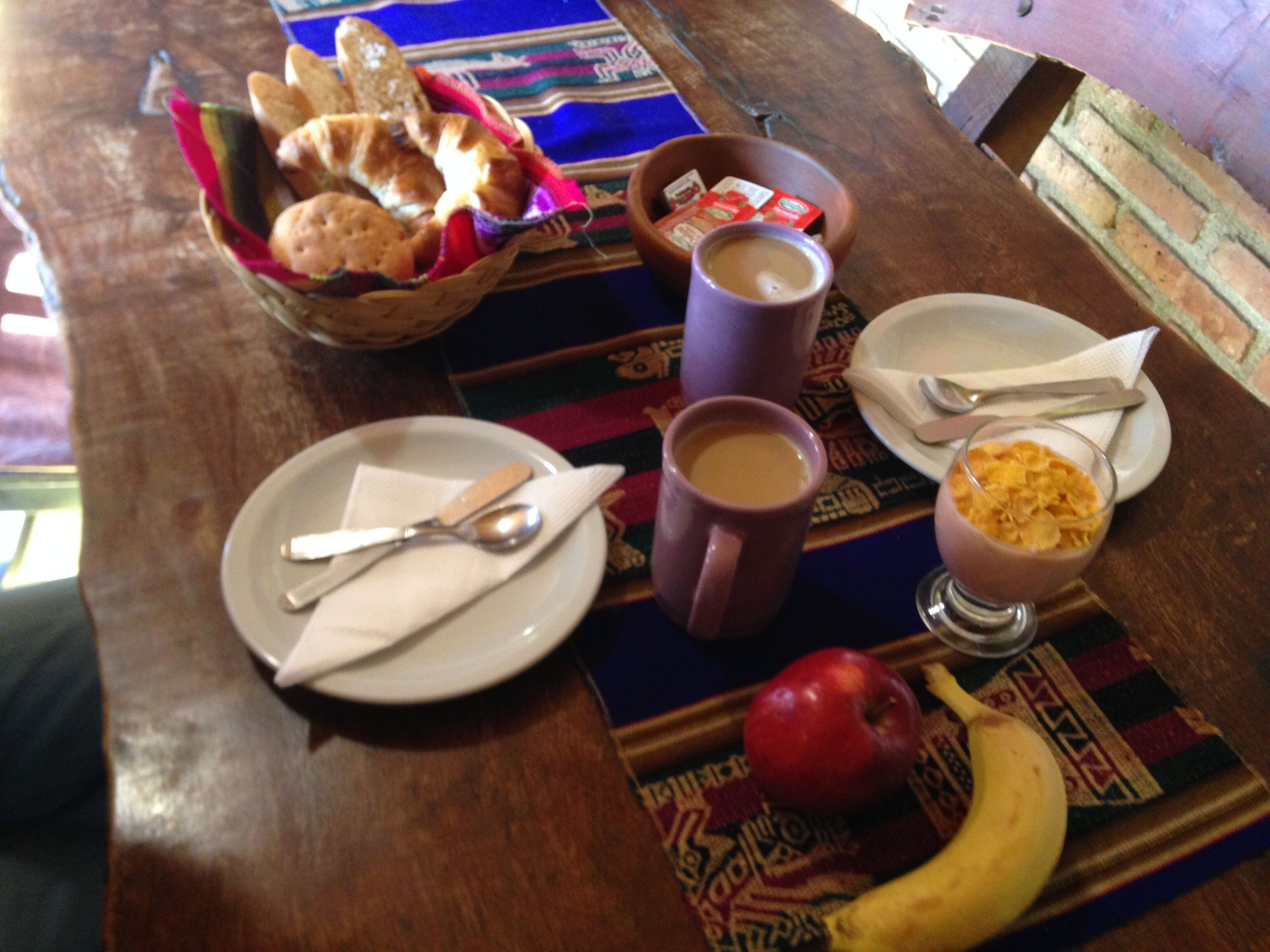 A dining table with a plate, spoon, mug, bowl, apple, and banana.