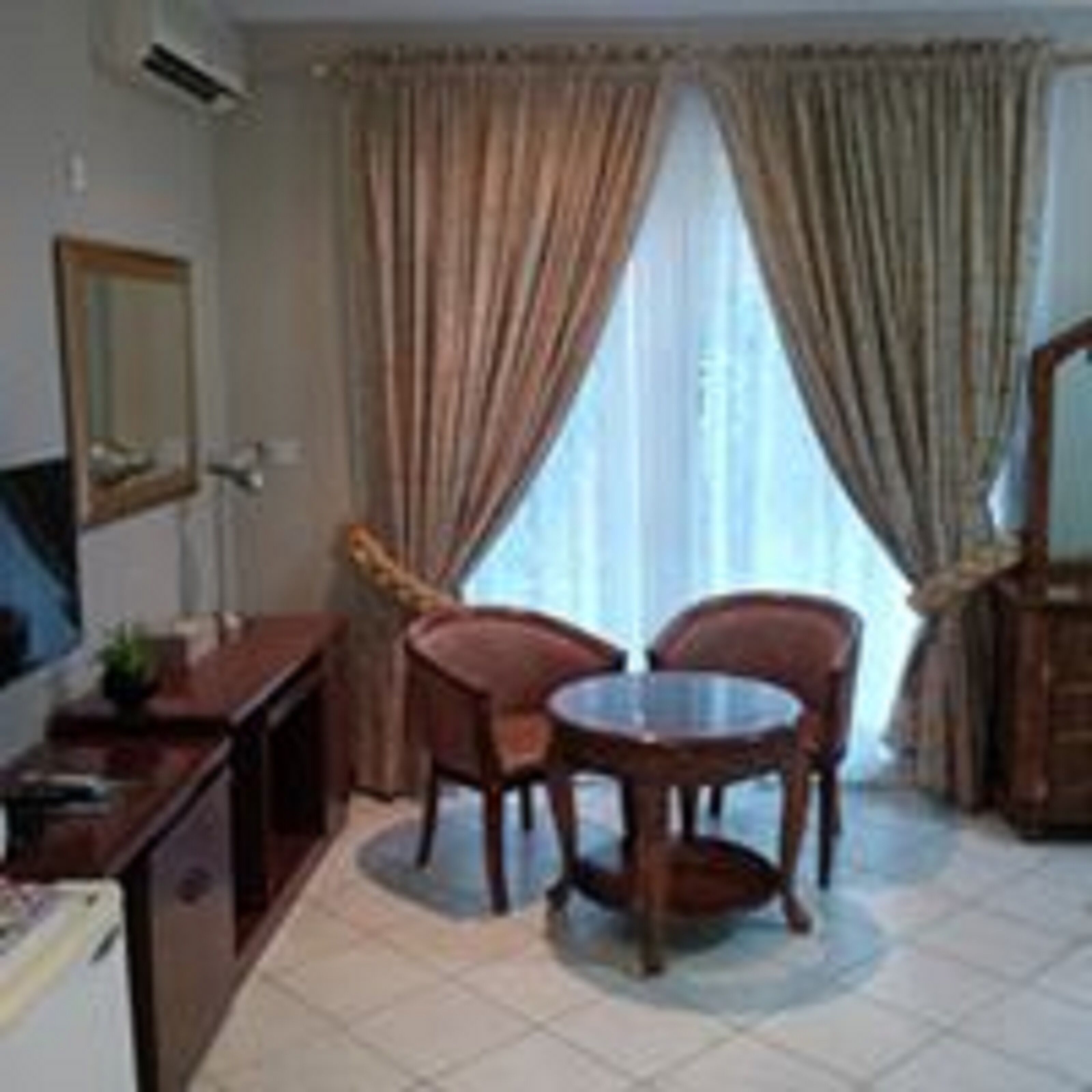 Habitación de hotel con cama, escritorio con silla, una pequeña mesa con dos sillas y una ventana con cortinas.
