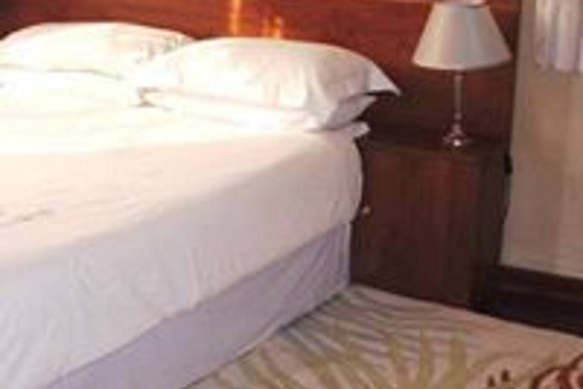 Un lit bien fait, avec du linge de lit blanc, une tête de lit en bois et une lampe de chevet posée sur une table de nuit.