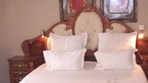 A neatly made bed with white linens and pillows, a wooden headboard, and a nightstand with a lamp.