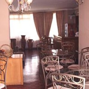 Un comedor con mesa y sillas de madera, una araña y vista a una sala con un piano.