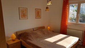 A bedroom with a wooden bed, two bedside lamps, a radiator, and two framed pictures on the wall.