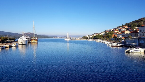 A marina with boats docked, a bridge in the background, and buildings along the waterfront.