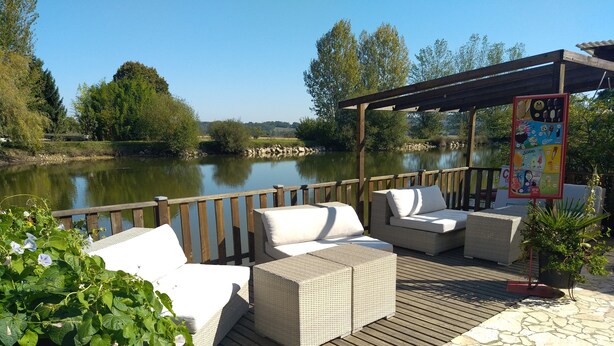 An outdoor seating area with wicker furniture and a wooden deck overlooking a body of water. - Paradise Chalets and Camping (Sarrecave)