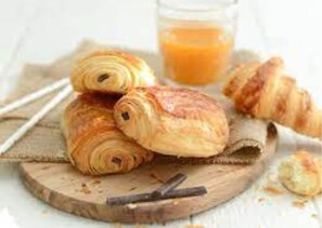 Cruasanes sobre una tabla de madera con un vaso de zumo de naranja al fondo.