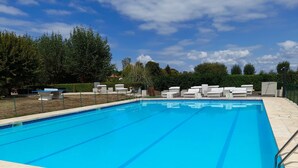 A rectangular swimming pool with clear blue water, surrounded by a stone deck. There are lounge chairs and a small seating area with a table and chairs. - Paradise Chalets and Camping (Sarrecave)