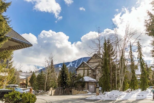 A mountain cabin with a snow-covered roof, surrounded by evergreen trees and a clear sky.