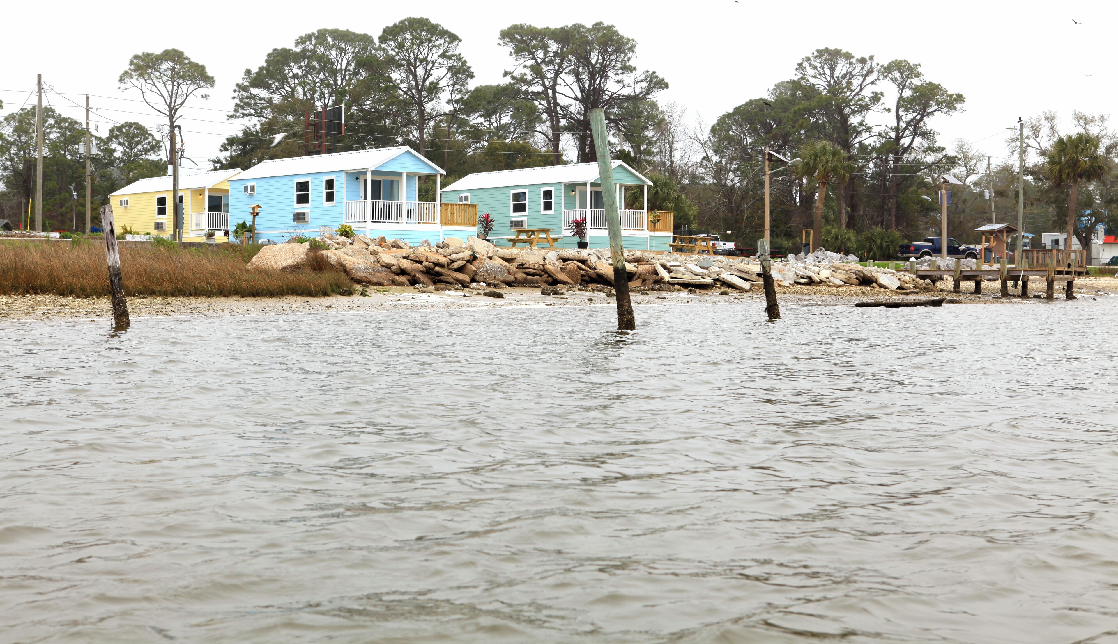 Une propriété située en bord de mer, avec une maison partiellement immergée, entourée d’arbres et bordée d’un rivage rocheux.