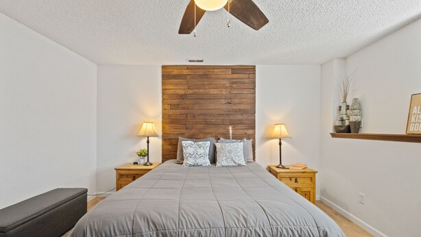 A bedroom with a wooden headboard, two bedside tables with lamps, a grey bedspread, and a ceiling fan. - Family space+ central +Private entry 2 Bedroom 1 Bath + Bunk Beds + Kitchen  (Colorado Springs)