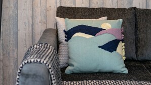 A room with a wooden wall, a black floor lamp, and a grey sofa with patterned cushions. - The Lucas - Donnini Apartments (Ayr)
