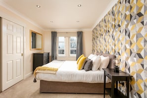 Une chambre à coucher comprenant un lit, une table de chevet, une commode et un mur orné d’un motif géométrique.